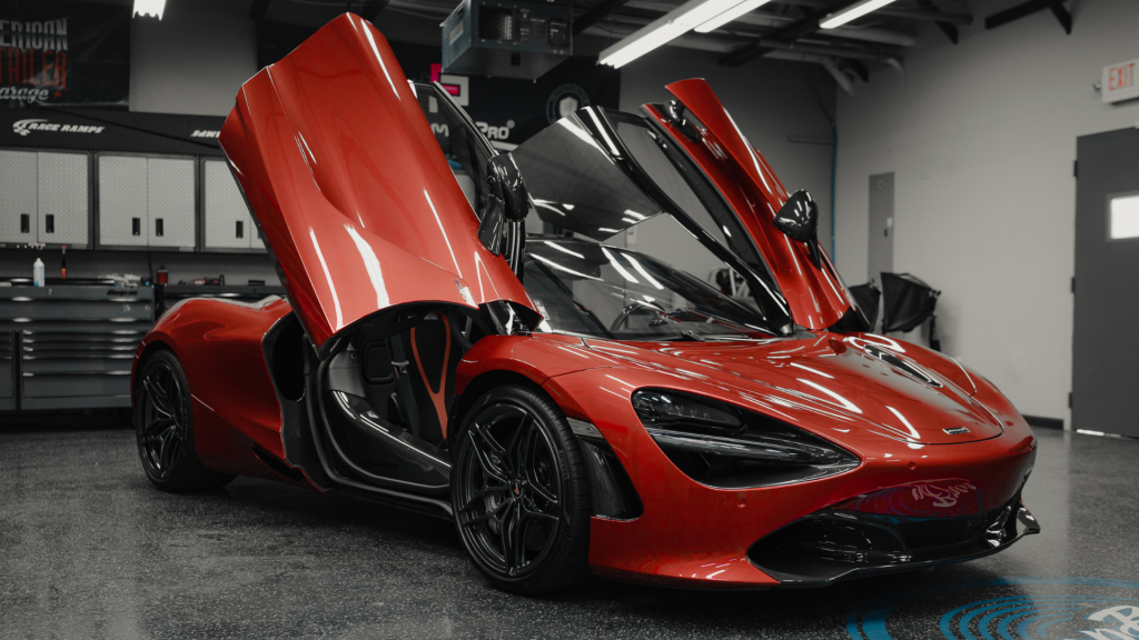 A striking red supercar with dramatic butterfly doors open wide sits in a pristine garage, showcasing its sleek, aggressive lines and high-performance allure.