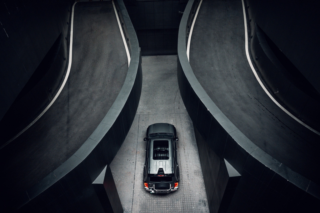 luxurious black Rolls-Royce descending a shadowy urban ramp, captured from an aerial or high vantage point.