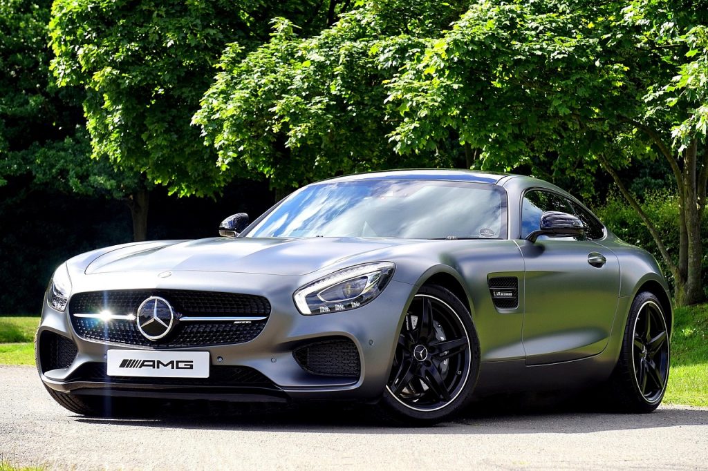 A matte grey Mercedes-AMG GT exudes luxury and performance, parked under sunlit trees with an aggressive stance and signature AMG styling.
