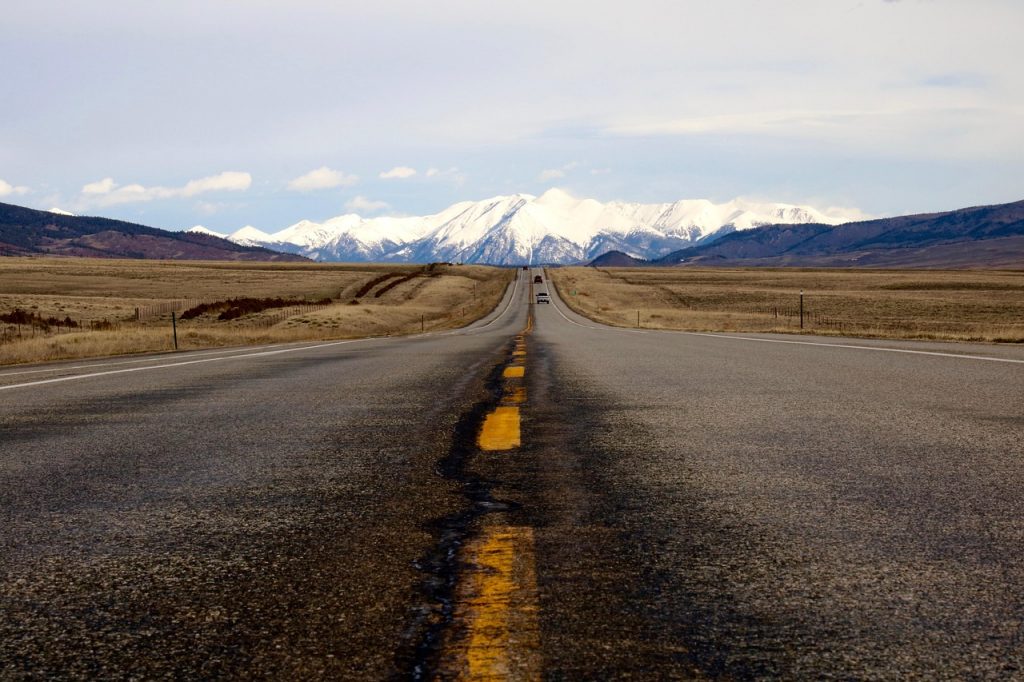 A quiet highway stretches toward snow-capped mountains, capturing the vastness and freedom of the open road.