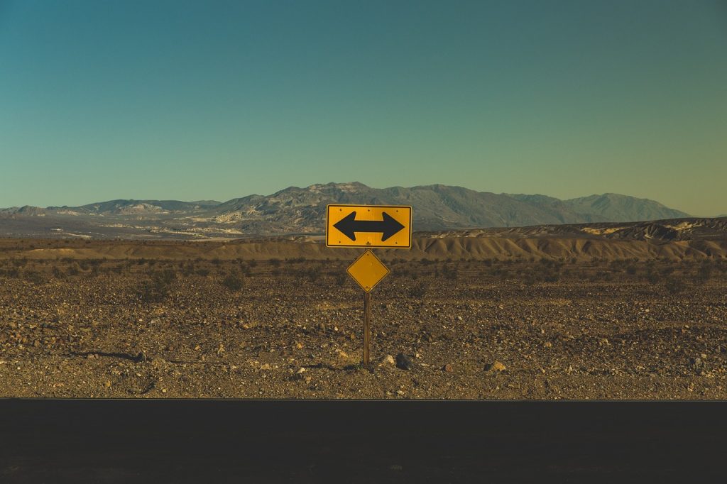 A yellow road sign with arrows pointing left and right stands in a barren desert landscape, symbolizing the critical decisions vehicle owners face—and how Ride Legal guides you to the right registration path.