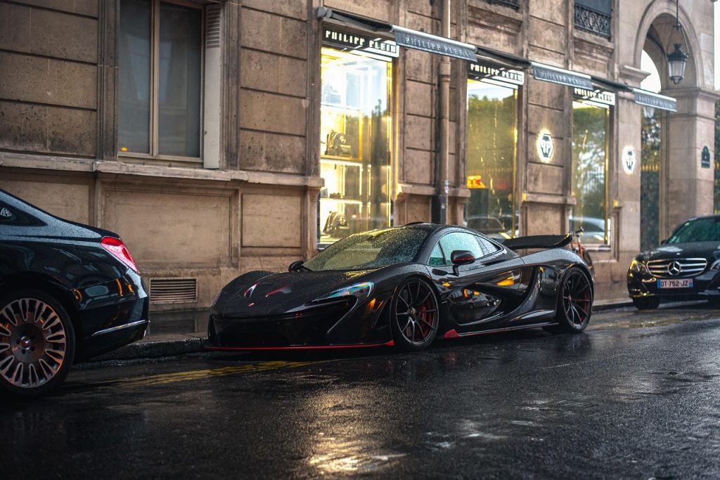 A black McLaren P1 sits parked on a rain-slicked European street, a perfect example of the kind of exotic vehicle that benefits from streamlined supercar registration services.