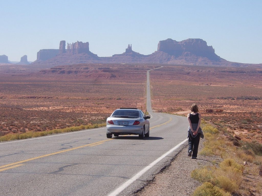 Woman walking next to parked car on desert highway toward Monument Valley, symbolizing tax-free freedom with Montana vehicle registration.