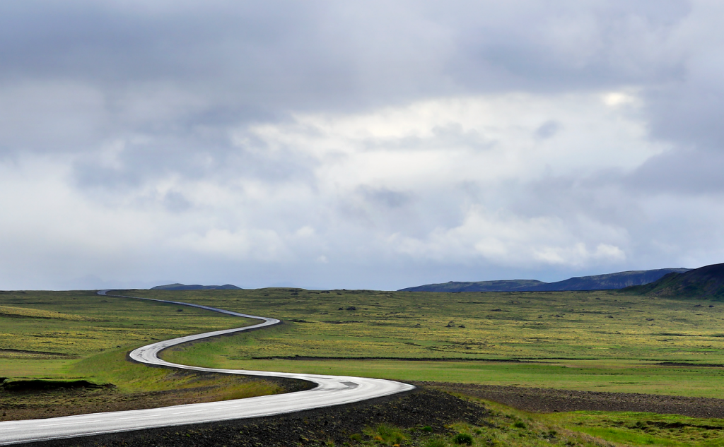 A winding road stretches through a vast, green landscape under a moody sky, symbolizing the open possibilities and peace of mind that Ride Legal’s vehicle registration services provide for any journey.