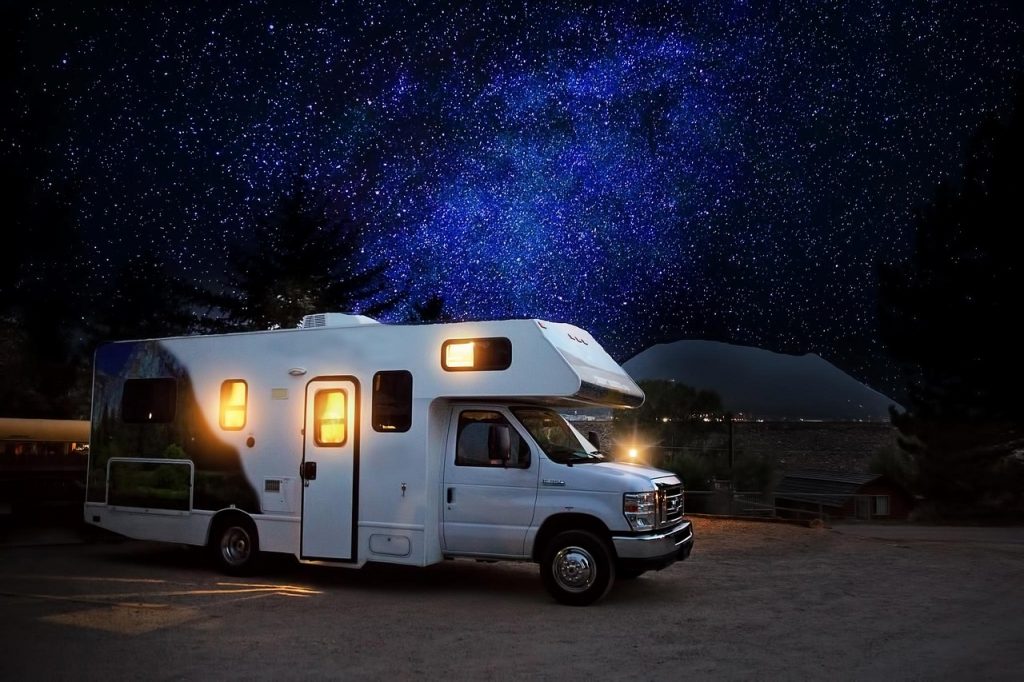 A white motorhome glows warmly under a star-filled Montana sky, symbolizing the freedom of the open road and the savings you can enjoy by registering in Montana.