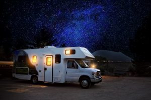 A white motorhome glows warmly under a star-filled Montana sky, symbolizing the freedom of the open road and the savings you can enjoy by registering in Montana.