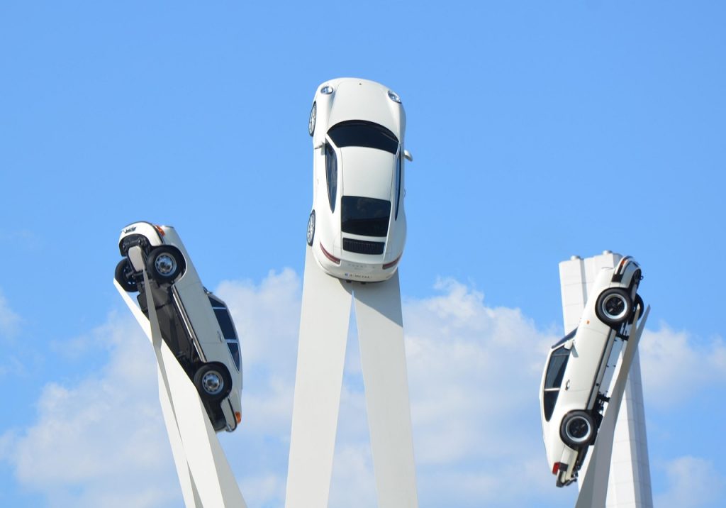 A striking sculpture displays three Porsche cars mounted on tall beams, appearing to soar into the sky as a tribute to the brand’s heritage and innovation.