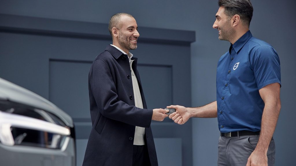 A smiling customer receives a car key from a dealership employee, symbolizing the completion of a successful vehicle transaction.